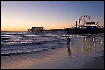 Couple reflected in wet sand at sunset, with pier and Ferris Wheel behind. Santa Monica, Los Angeles, California, USA