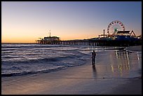 Couple reflected in wet sand at sunset, with pier and Ferris Wheel behind. Santa Monica, Los Angeles, California, USA (color)