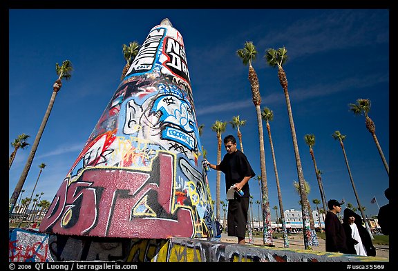 Man painting inscriptions on a graffiti-decorated tower. Venice, Los Angeles, California, USA (color)