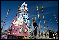 Man painting inscriptions on a graffiti-decorated tower. Venice, Los Angeles, California, USA (color)
