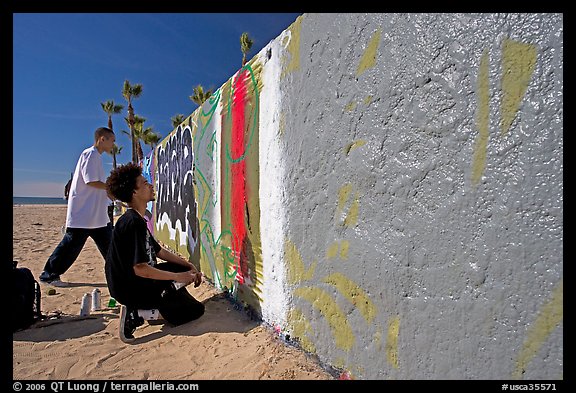 Young men creating graffiti art on a wall on the beach. Venice, Los Angeles, California, USA