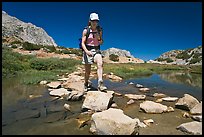 Woman crossing stream on rocks, John Muir Wilderness. California, USA