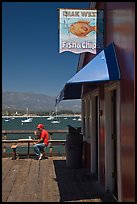 Man eating on wharf next to Fish and Chips restaurant. Santa Barbara, California, USA