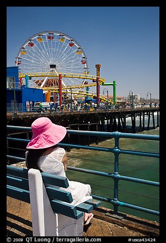 Woman sitting on bench with pink hat and ferris wheel. Santa Monica, Los Angeles, California, USA