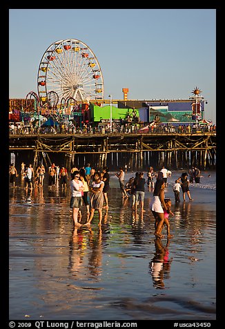 Pier and beachgoers reflected in wet sand, late afternoon. Santa Monica, Los Angeles, California, USA