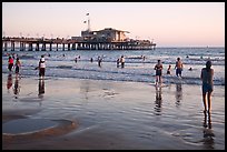 Beachgoers near Santa Monica Pier reflected in wet sand, sunset. Santa Monica, Los Angeles, California, USA