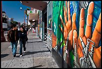 Couple walks past mural on Mission street, Mission District. San Francisco, California, USA ( color)