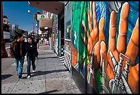 Couple walks past mural on Mission street, Mission District. San Francisco, California, USA (color)