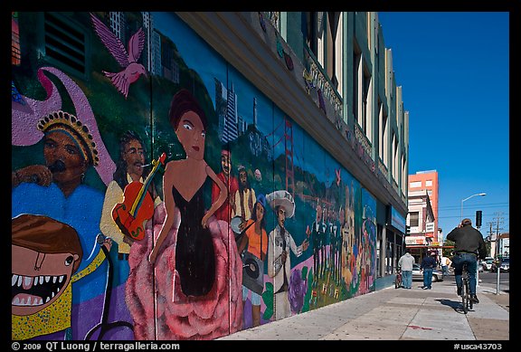 Man riding bicycle on sidewalk past mural, Mission District. San Francisco, California, USA