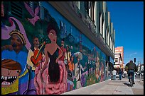 Man riding bicycle on sidewalk past mural, Mission District. San Francisco, California, USA (color)