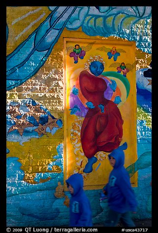 Boys in blue hooded jackets walk past mural, Mission District. San Francisco, California, USA (color)