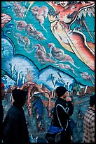 Men in dark jackets walk past mural, Mission District. San Francisco, California, USA