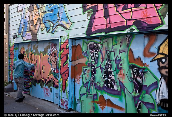 Man hanging poster on painted garage door, Mission District. San Francisco, California, USA (color)