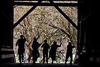 Silhouettes of dancers with sticks inside covered bridge, Felton. California, USA