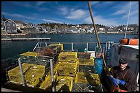 Lobsterman in boat with traps, and village in background. Stonington, Maine, USA