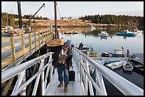 Man carrying construction wood and rolling case out of mailboat. Isle Au Haut, Maine, USA ( color)