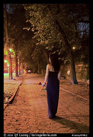 Woman in evening dress with rose on alley bordering Central Park at night. NYC, New York, USA