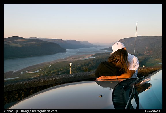 Couple embracing on car hood, with view of mouth of river gorge. Columbia River Gorge, Oregon, USA