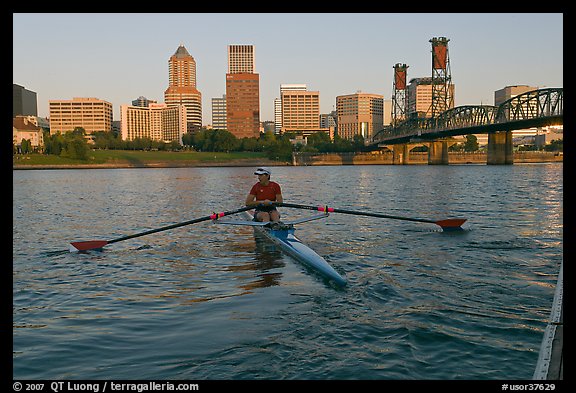 Woman rowing on racing shell and city skyline at sunrise. Portland, Oregon, USA (color)