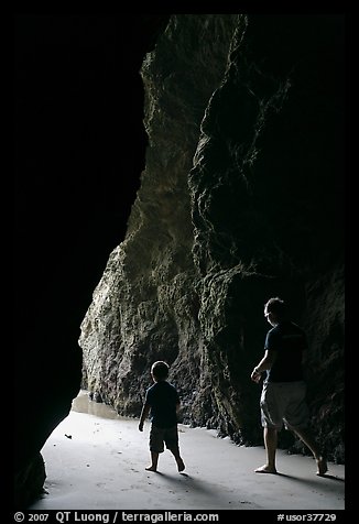 Father and son walking towards the light in sea cave. Bandon, Oregon, USA