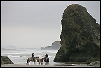 Women ridding horses next to sea stack. Bandon, Oregon, USA