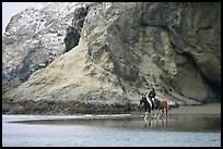 Woman horse-riding on beach next to sea cave entrance. Bandon, Oregon, USA