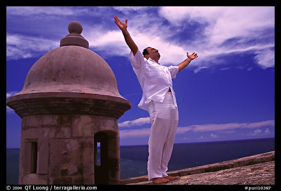 Man standing next to a lookout turret, with arms spread, El Morro Fortress. San Juan, Puerto Rico (color)