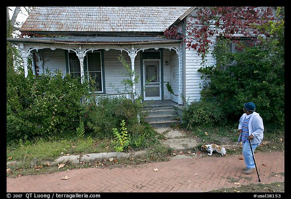 Woman walking dog in front of a crooked house. Selma, Alabama, USA (color)