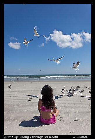 Girl sitting on beach with birds flying, Jetty Park. Cape Canaveral, Florida, USA