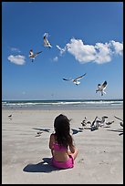 Girl sitting on beach with birds flying, Jetty Park. Cape Canaveral, Florida, USA