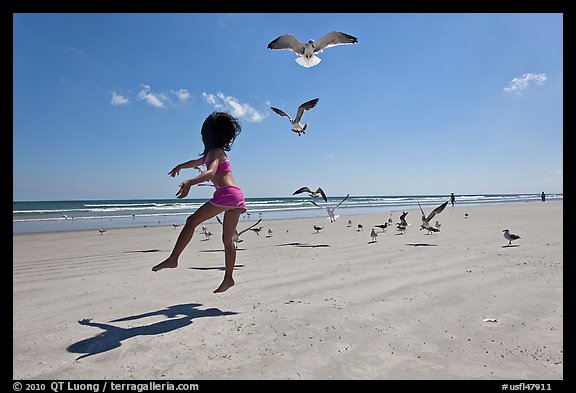 Girl jumping on beach with seagulls flying, Jetty Park. Cape Canaveral, Florida, USA (color)