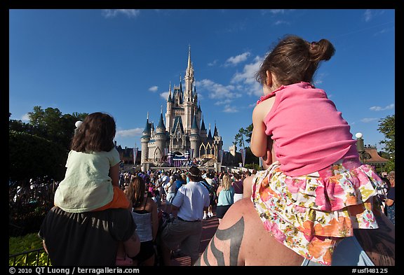 Toddlers sit on parent shoulders druing stage show. Orlando, Florida, USA