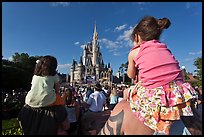 Toddlers sit on parent shoulders druing stage show. Orlando, Florida, USA (color)
