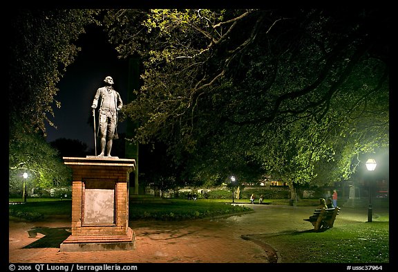 Park with statue and couples sitting on public benches at night. Charleston, South Carolina, USA