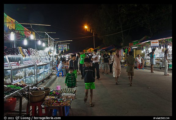 Shoppers walk past craft booth at night market. Phu Quoc Island, Vietnam