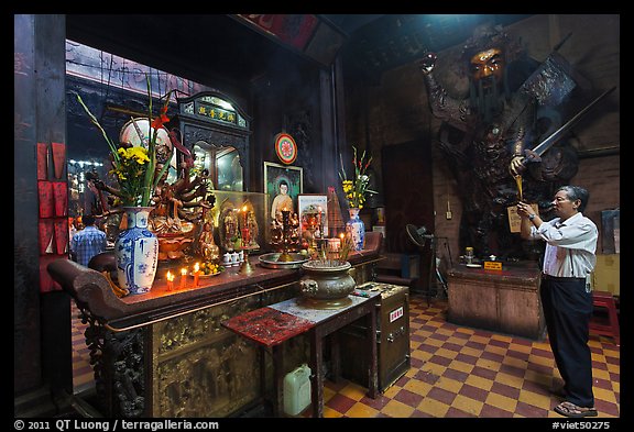 Man in prayer, with fierce statue of general behind, Jade Emperor Pagoda, district 3. Ho Chi Minh City, Vietnam