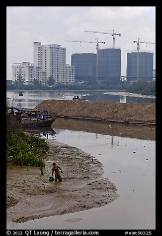 Man wading in mud, with background of towers in construction, Phu My Hung, district 7. Ho Chi Minh City, Vietnam