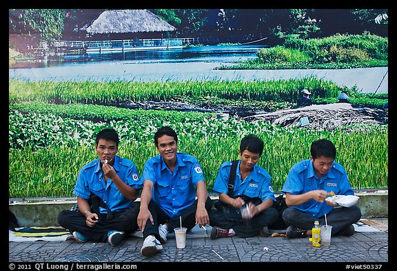 Uniformed students eating in front of backdrop depicting rural landscape. Ho Chi Minh City, Vietnam (color)