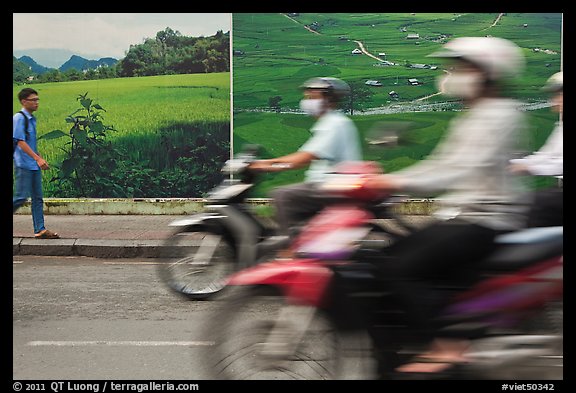 Man walking and motorbike riders blured in front of backdrops depicting traditional landscapes. Ho Chi Minh City, Vietnam