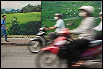 Man walking and motorbike riders blured in front of backdrops depicting traditional landscapes. Ho Chi Minh City, Vietnam