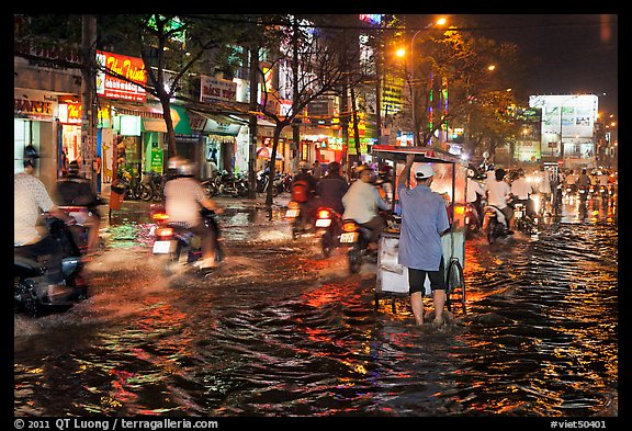 Traffic passes man pushing food cart on flooded street at night. Ho Chi Minh City, Vietnam (color)