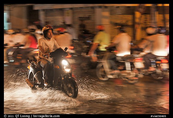 Man riding motorbike on flooded street seen against riders going in opposite direction. Ho Chi Minh City, Vietnam (color)