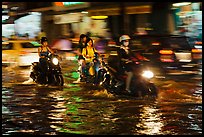 Women riding motorcyles at night in water. Ho Chi Minh City, Vietnam