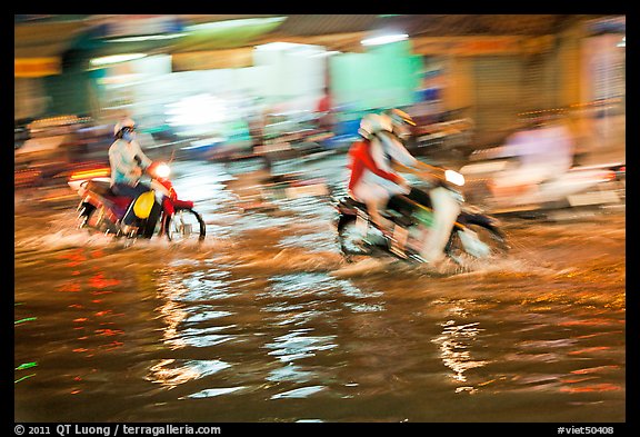 Motion-blured exposure of riders on flooded street at night. Ho Chi Minh City, Vietnam (color)