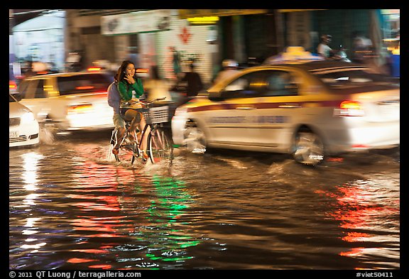 Women riding a bicycle on a flooded street at night. Ho Chi Minh City, Vietnam (color)