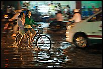 Women sharing a bicycle ride at night on a water-filled street. Ho Chi Minh City, Vietnam (color)