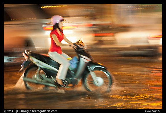 Woman riding on water-filled street, and light streaks. Ho Chi Minh City, Vietnam