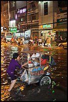 Vendor pushing foot car into the water at night. Ho Chi Minh City, Vietnam