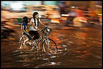 Girls sharing night bicycle ride through water of flooded street. Ho Chi Minh City, Vietnam