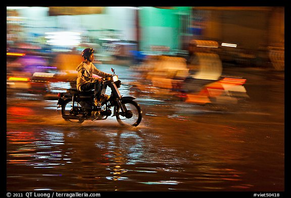 Motorcyclist speeding on wet street at night, with streaks giving sense of motion. Ho Chi Minh City, Vietnam (color)